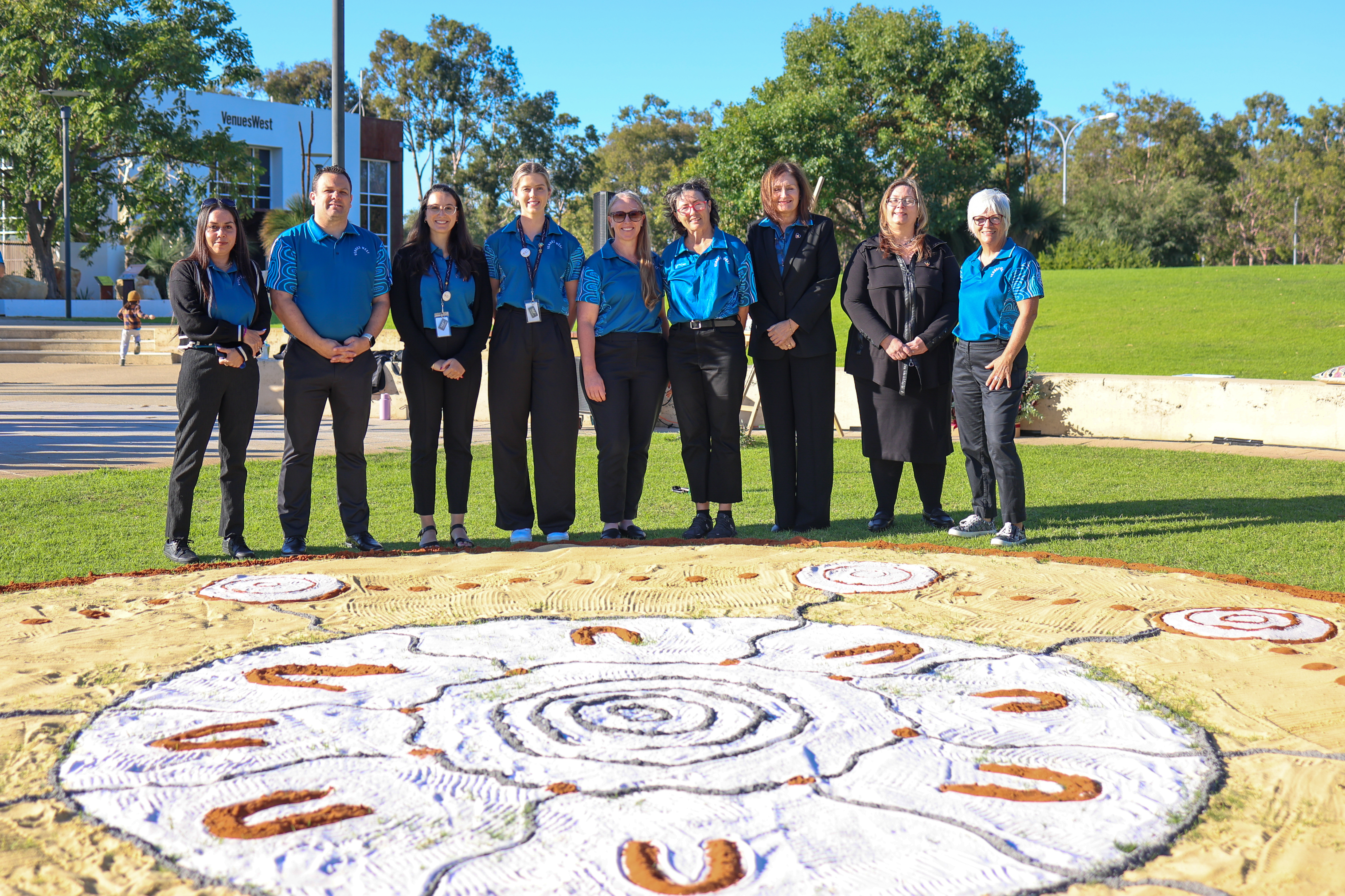 A photo of VenuesWest employees in front of Indigenous artwork